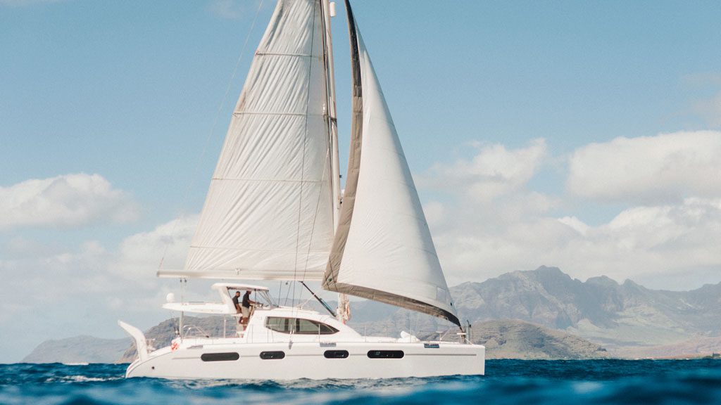 Sailboat on ocean with mountains in background on a clear day.