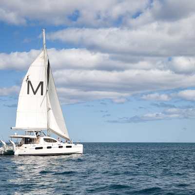 Sailboat with 'M' on sail cruising on blue sea under cloudy sky.