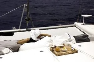 Person relaxing on yacht deck with drink tray near ocean.