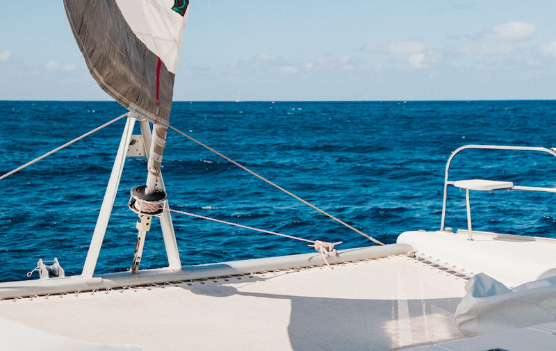 View from a sailboat deck with sail and blue ocean under a clear sky.