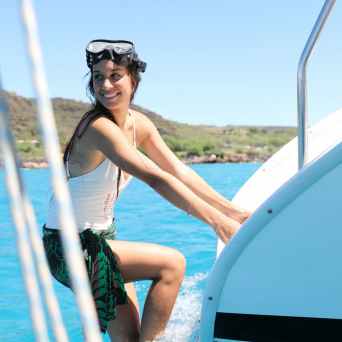 Woman in swimwear climbing boat ladder from clear blue water.